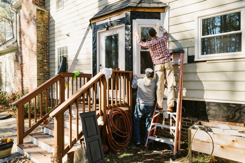 Two construction workers are repairing storm damage to a house’s exterior siding in Akron, OH